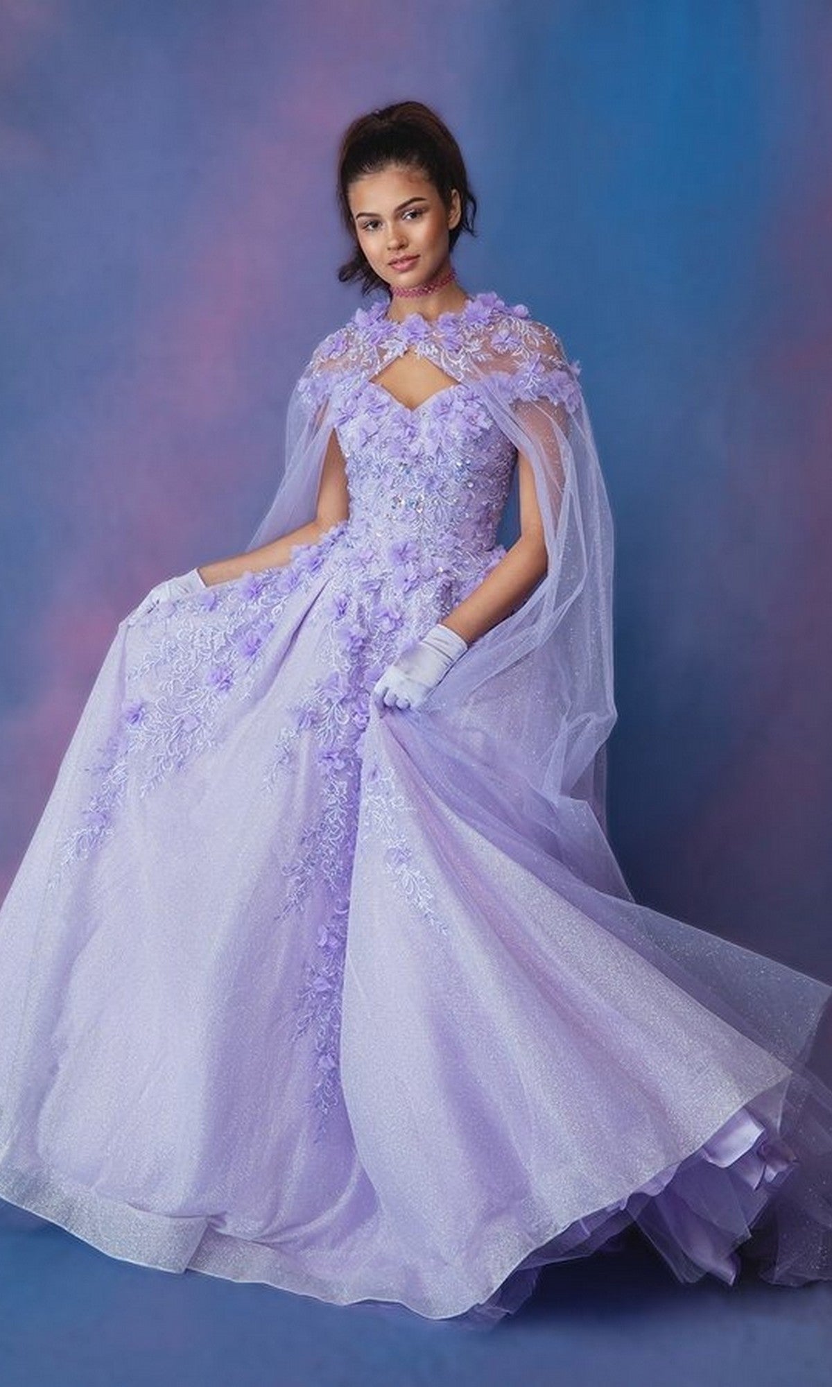 A woman models the Long Prom Dress: Eureka 9339, featuring glitter fabric, 3D floral appliques, and a detachable tulle cape, posed against a gradient blue and purple background.
